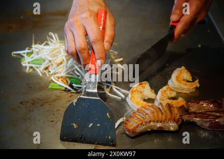 mains du chef avec spatule sur teppanyaki. cuisson des légumes, de la viande et des fruits de mer sur une table chaude à griller hibachi. Japonais traditionnel. Spectacle Teppan. cuisine Banque D'Images