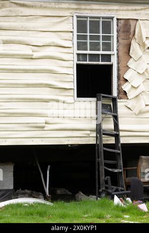 Une fenêtre extérieure ouverte avec un revêtement de vinyle en plastique endommagé et fondu recouvert de suie sale sur une maison qui avait un feu intérieur chaud. Banque D'Images