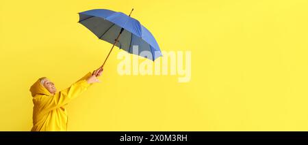 Belle femme mature en imperméable et avec parapluie sur fond jaune avec espace pour le texte Banque D'Images