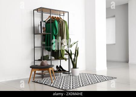 Rack avec vêtements féminins élégants, chaussures et plante d'intérieur à l'intérieur de la pièce lumineuse Banque D'Images