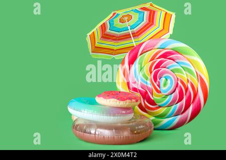 Anneaux gonflables, matelas de natation en forme de bonbons et parasol sur fond vert Banque D'Images