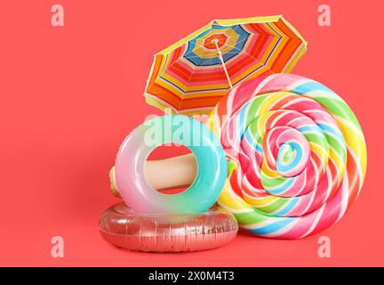 Anneaux gonflables, matelas de natation en forme de bonbons et parasol sur fond rouge Banque D'Images