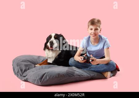 Petit garçon avec chien de montagne bernois jouant au jeu vidéo sur fond rose Banque D'Images