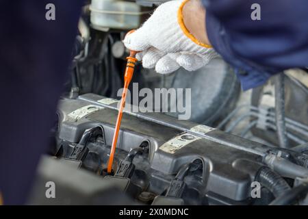 Gros plan de la main de mécanicien avec gant de protection vérifiant le niveau d'huile d'une voiture. Entretien de routine de la voiture pour un fonctionnement sûr et efficace du moteur. Banque D'Images