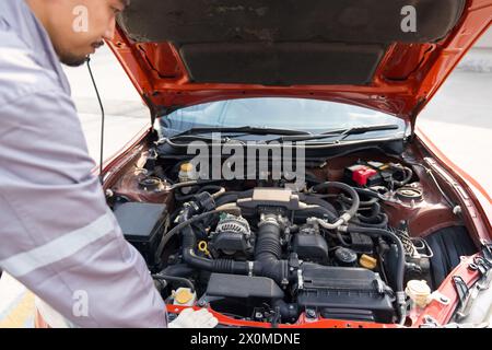 Un mécanicien en uniforme et gant de protection regarde le moteur d'une voiture de sport pour le réparer. Atmosphère de travail à l'atelier de réparation de voiture. Banque D'Images