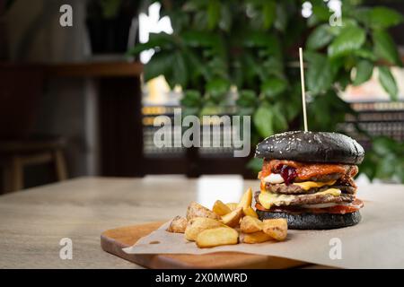 délicieux burger noir frais avec fromage et sauce tomate servi avec des frites sur une planche de bois dans le café Banque D'Images