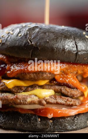 Gros plan d'un double grand burger avec ketchup de tomate et fromage sur un pain noir. Prise de vue macro Banque D'Images