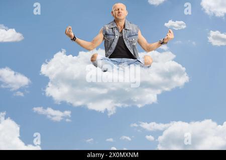 Homme chauve assis les jambes corssées et pratiquant la méditation dans le ciel sur un nuage Banque D'Images