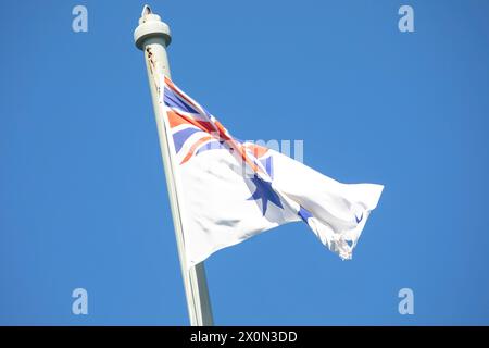 Drapeau australien White Ensign volant au sommet du mât commémoratif HMAS Sydney 1 au fort Bradleys Head sur la rive nord de Sydney, Nouvelle-Galles du Sud, Australie Banque D'Images