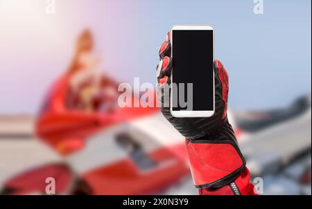 Smartphone Biker portable avec écran vierge, image rognée, espace de copie, écran vide pour le design graphique avec une moto en arrière-plan Banque D'Images