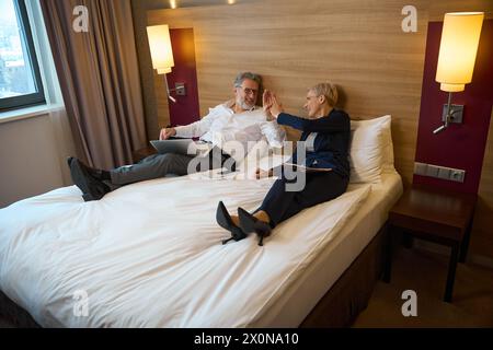 Homme d'affaires heureux et femme d'affaires se donnant cinq l'un l'autre pendant le travail sur le lit Banque D'Images