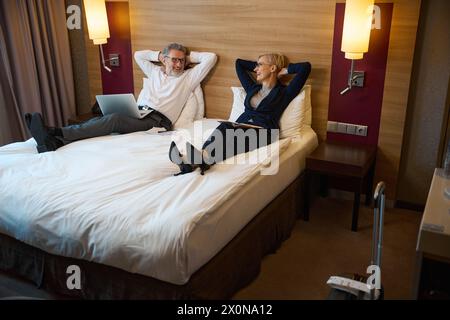 Joyeux homme d'affaires et femme d'affaires se reposant et se regardant sur le lit Banque D'Images