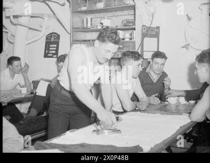 Les Royal Marines non surveillés pendant une accalmie dans les opérations se détendent en écrivant des lettres, en repassant des vêtements ou en jouant à des jeux, montrant la vie quotidienne à bord des navires de la Royal Navy pendant la seconde Guerre mondiale. Banque D'Images
