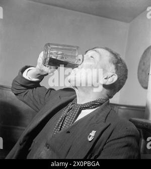 WARTIME PUB : LA VIE QUOTIDIENNE AU WYNNSTAY ARMS, RUABON, DENBIGHSHIRE, PAYS DE GALLES, ROYAUME-UNI, 1944 - L'ouvrier local Price Evans boit sa pinte de bière au Wynnstay Arms à Ruabon. Selon la légende originale, M. Evans a dit : « C'est peut-être cher, c'est peut-être mince, mais il n'y a pas de mauvaise bière » Banque D'Images