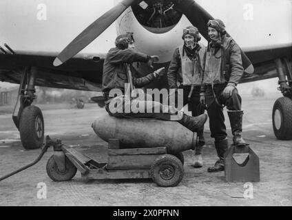 HUITIÈME FORCE AÉRIENNE DES ÉTATS-UNIS EN GRANDE-BRETAGNE, 1942-1945 - le lieutenant George F. perpente, assis sur un chariot chargé de bombes, parle au lieutenant Francis N. King et au lieutenant William Thistlewaite, également du 353e groupe de chasse. Le groupe est devant un P-47 Thunderbolt. Cette photographie a été prise à la base aérienne de Metfield où le groupe était stationné entre le 3 août 1943 et le 12 avril 1944. Adopté pour publication le 4 décembre 1943.légende imprimée au verso : 'les chasseurs américains portent maintenant des bombes. Les photos montrent : les pilotes de chasse américains discutent de leur premier raid de chasseur bombardier en attendant leurs Thunderbolt Banque D'Images