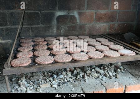 Un gril plein de hamburgers cuit sur un four en briques. Les burgers sont tous de tailles différentes et sont cuits sur une grille métallique. La scène a de la rouille Banque D'Images