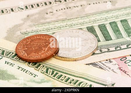 Pièces de monnaie avec l'image d'Elizabeth II. Pièces anglaises blanches et jaunes sur le fond des billets de dollars vue de dessus. Banque D'Images