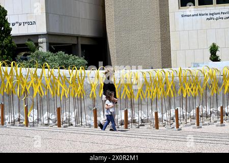 Tel Aviv, Israël. 13 avril 2024. Une femme marche avec un enfant devant des sculptures en ruban jaune pour des otages israéliens retenus captifs à Gaza par le Hamas, sur la place des otages à tel Aviv, le samedi 13 avril 2024. Photo de Debbie Hill/ crédit : UPI/Alamy Live News Banque D'Images