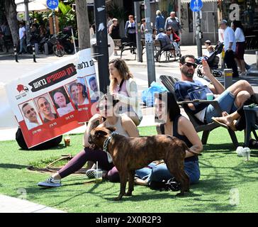 Tel Aviv, Israël. 13 avril 2024. Les gens profitent d’une journée ensoleillée près d’une bannière avec des photos d’otages israéliens retenus captifs à Gaza par le Hamas, dans une rue de tel Aviv, le samedi 13 avril 2024. Photo de Debbie Hill/ crédit : UPI/Alamy Live News Banque D'Images