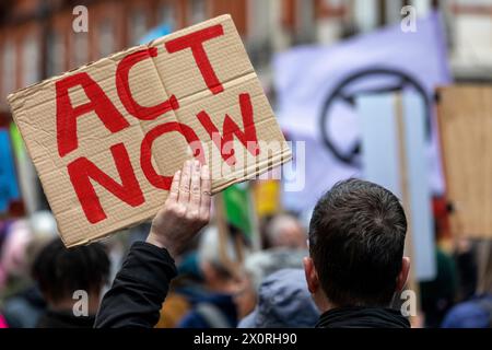 Un rassemblement contre le changement climatique dans le centre de Londres en 2022, avec un manifestant portant une pancarte en carton avec les mots « Act Now » écrits en rouge. Banque D'Images