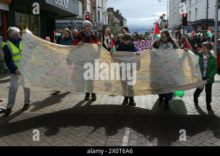 Rhyl, Royaume-Uni. 13 avril 2024. Les manifestants portent une banderole portant les noms de tous les civils palestiniens connus tués pendant la manifestation. Plus de 150 partisans pro-palestiniens de partout au pays de Galles ont manifesté dans les rues pour exiger un cessez-le-feu à Gaza et mettre fin au génocide. Crédit : SOPA images Limited/Alamy Live News Banque D'Images
