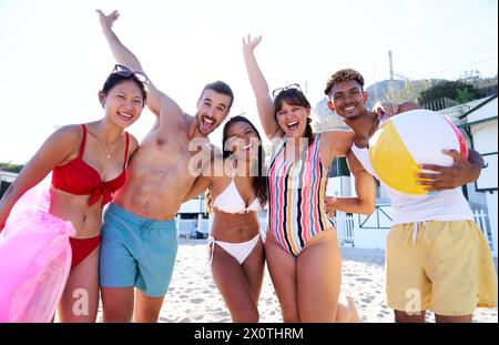 Portrait de cinq amis sur la plage s'amusant à regarder la caméra souriant et levant les bras. Banque D'Images
