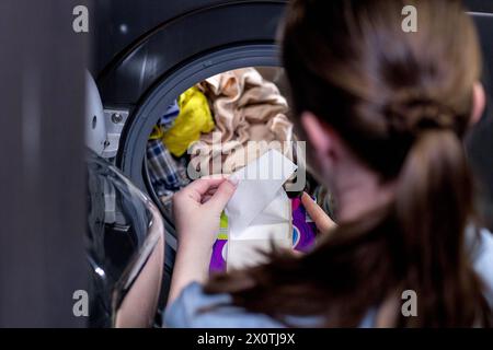 Femme assis devant une machine à laver chargeant des vêtements sales, serviettes pour laver des vêtements colorés. Banque D'Images