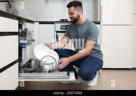 Homme souriant chargement lave-vaisselle avec des assiettes dans la cuisine Banque D'Images