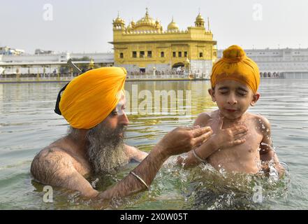 AMRITSAR, INDE - 13 AVRIL : un dévot sikh avec son enfant se baignent dans le Saint Sarovar (réservoir d'eau sacrée) à l'occasion du festival Baisakhi au Temple d'Or le 13 avril 2024 à Amritsar, Inde. Baisakhi ou Vaisakhi, une fête populaire du printemps qui marque le premier jour du mois du Vaisakh, est célébrée avec beaucoup d'enthousiasme parmi les communautés hindoue, sikhe et bouddhiste. C'est le début du nouvel an pendjabi et sikh qui est célébré dans toute l'Inde, en particulier au Punjab et dans le nord de l'Inde. Baisakhi est observé le 13 avril de cette année, annonçant le début de la saison de récolte à Punja Banque D'Images