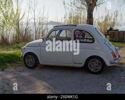 Fiat 500 classique en blanc garé au bord du lac Bolsena près de Montefiascone par une soirée ensoleillée. Province de Viterbe, région du Latium, Italie. 13 avril 2024 Banque D'Images