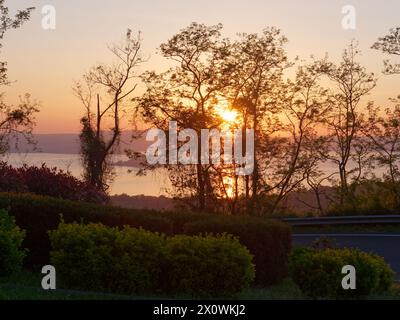 Coucher de soleil Pver lac Bolsena vu à travers les arbres sur la route de la 'via del Lago' province de Viterbo, région du Latium, Italie. 13 avril 2024 Banque D'Images