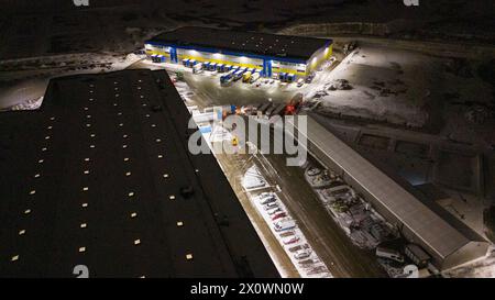 Photographie par drone de l'entrepôt logistique et des camions garés pendant la nuit nuageuse d'hiver Banque D'Images