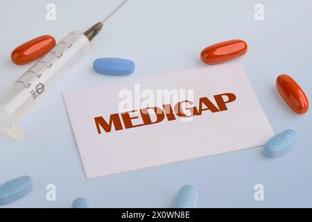 Concept médical. MEDIGAP sur une carte de visite blanche sur fond bleu à côté d'une seringue, pilules, vitamines Banque D'Images