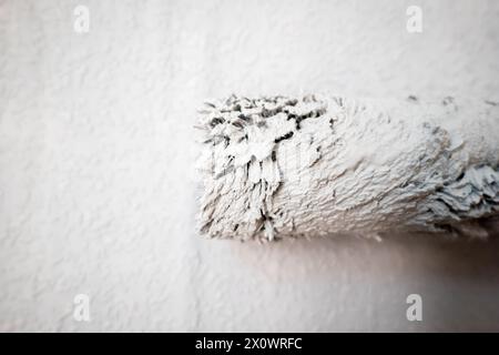 Rouleau de peinture mât extensible sur le mur de papier peint en copeaux de bois peint peint peint pendant la rénovation de la maison en angleterre royaume-uni. Banque D'Images