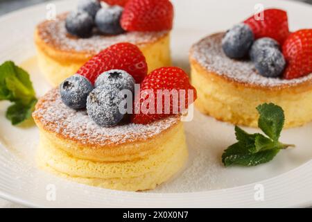 Les crêpes japonaises sont des crêpes moelleuses, ressemblant à un souffle, qui sont à la perfection aérée lorsqu'elles sont recouvertes de sucre en poudre, de myrtilles et de fraises gros plan sur un p. Banque D'Images