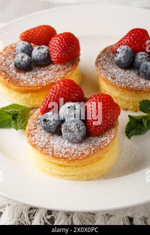 Les crêpes de soufflé japonais moelleuses sont comme manger des nuages cotonneux avec des baies fraîches en gros plan sur une assiette sur la table. Vertical Banque D'Images