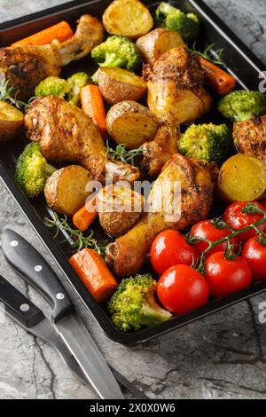 Pilon de poulet cuit au four avec brocoli, pommes de terre, tomates et carottes gros plan sur une poêle sur la table. Vertical Banque D'Images