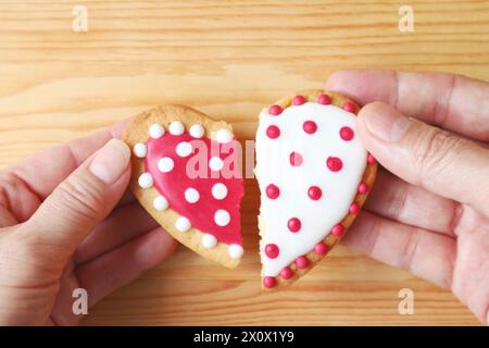 La main de la femme et la main de l'homme tenant deux demi-biscuits en forme de coeur attachent sur fond de bois Banque D'Images