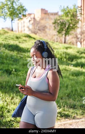 femme afro-américaine sinueuse marchant dans des vêtements de sport écoutant de la musique Banque D'Images