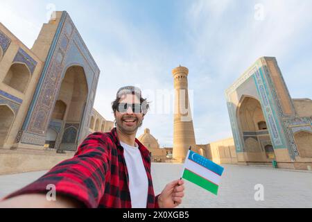 Heureux touriste voyageant en Ouzbékistan prendre une photo selfie avec le drapeau de l'ouzbékistan devant le minaret Kalyan et la mosquée, Boukhara, Ouzbékistan. Banque D'Images