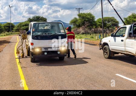 hommes africains réparant et entretenant les marquages routiers délavés sur l'autoroute, repeignant les marquages jaunes pour la sécurité routière Banque D'Images