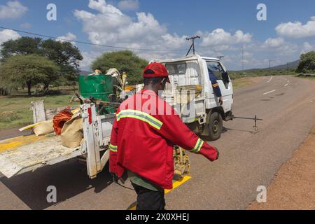 hommes africains réparant et entretenant les marquages routiers délavés sur l'autoroute, repeignant les marquages jaunes pour la sécurité routière Banque D'Images