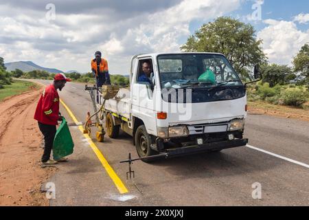 hommes africains réparant et entretenant les marquages routiers délavés sur l'autoroute, repeignant les marquages jaunes pour la sécurité routière Banque D'Images