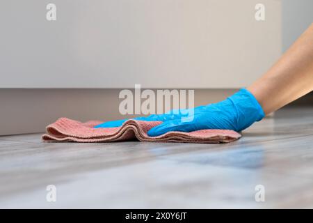 femme au foyer en gants de caoutchouc lave le sol à la maison. femme faisant le nettoyage humide à la maison. l'homme lave le sol près du placard. Banque D'Images