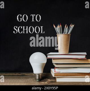 Un tableau noir avec les mots Go to School écrits dessus. Une ampoule est sur le dessus des livres et un porte-crayon est sur le dessus des livres Banque D'Images