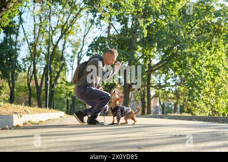 homme avec son chiot mignon dans un pull dans le parc de formation, se nourrir, sourire. Printemps, été, automne bel homme s'amusant avec son chien en plein air. SPAC Banque D'Images