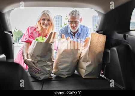 Les aînés joyeux regardent dans le coffre de voiture après avoir magasiné Banque D'Images