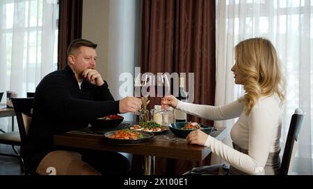 Un couple festif porte un toast dans un restaurant. Un jeune couple romantique partage un toast, serrant des verres de vin rouge et regardant attentivement Banque D'Images