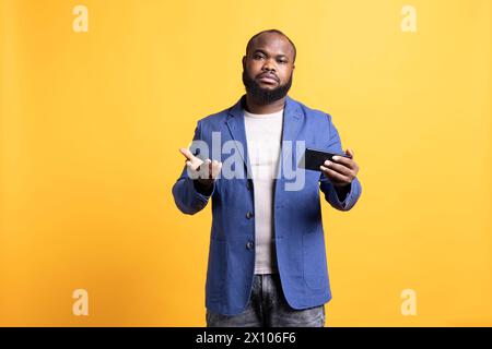 Portrait de l'homme déçu malheureux après avoir reçu de mauvaises nouvelles d'un ami, parlant sur smartphone. Triste personne du BIPOC froncant les sourcils après avoir lu des messages texte sur le téléphone, fond de studio Banque D'Images