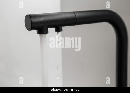L'eau coule du robinet noir dans la cuisine. Banque D'Images